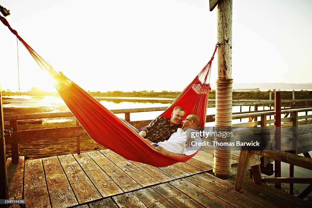 Gay couple in hammock on dock at sunset