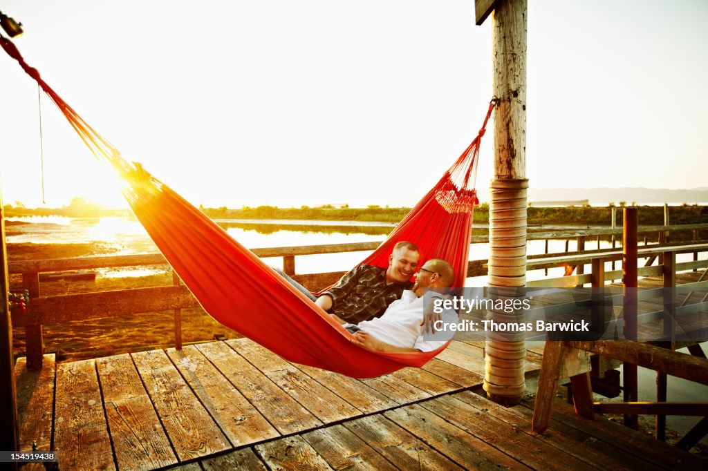 Gay couple in hammock on dock at sunset