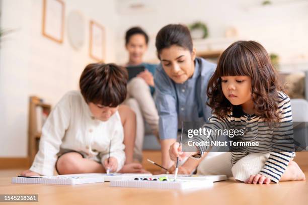 sharpen creativity skills and self-confidence in childhood with watercolor painting activities.  a boy and sister are painting with watercolor paint on a hardwood floor while the mother is advice behind in the living room. - emotional intelligence stock pictures, royalty-free photos & images