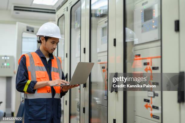 asian electrical technician worker with personal safety equipment using laptop computer operating or check status from control panel switch board in control room of high voltage electric transformer station. industrial business occupation worker concept. - electrical switch board stock pictures, royalty-free photos & images