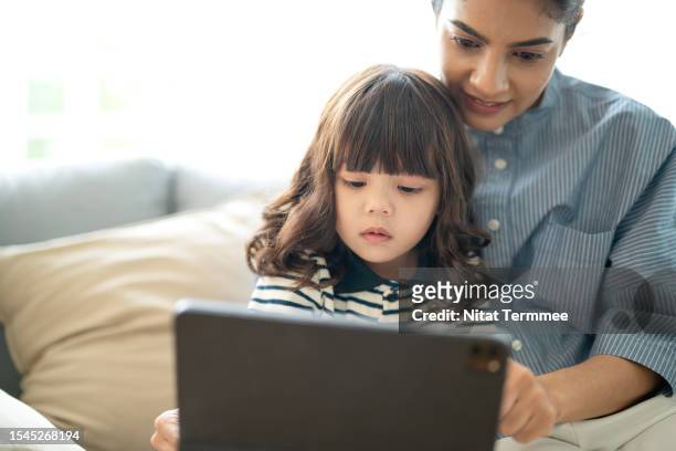 digital learning and transformation of education, parent, and family in digital learning. a mother assisting on homework to her daughter using a digital tablet in the living room. - children screen stock-fotos und bilder