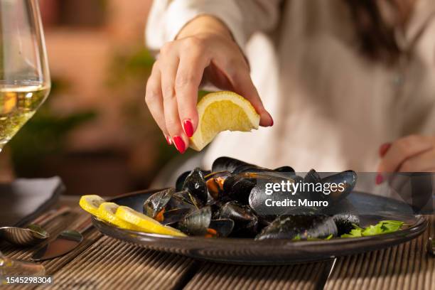 young woman pouring lemon juice on steamed mussels - mussels stock pictures, royalty-free photos & images