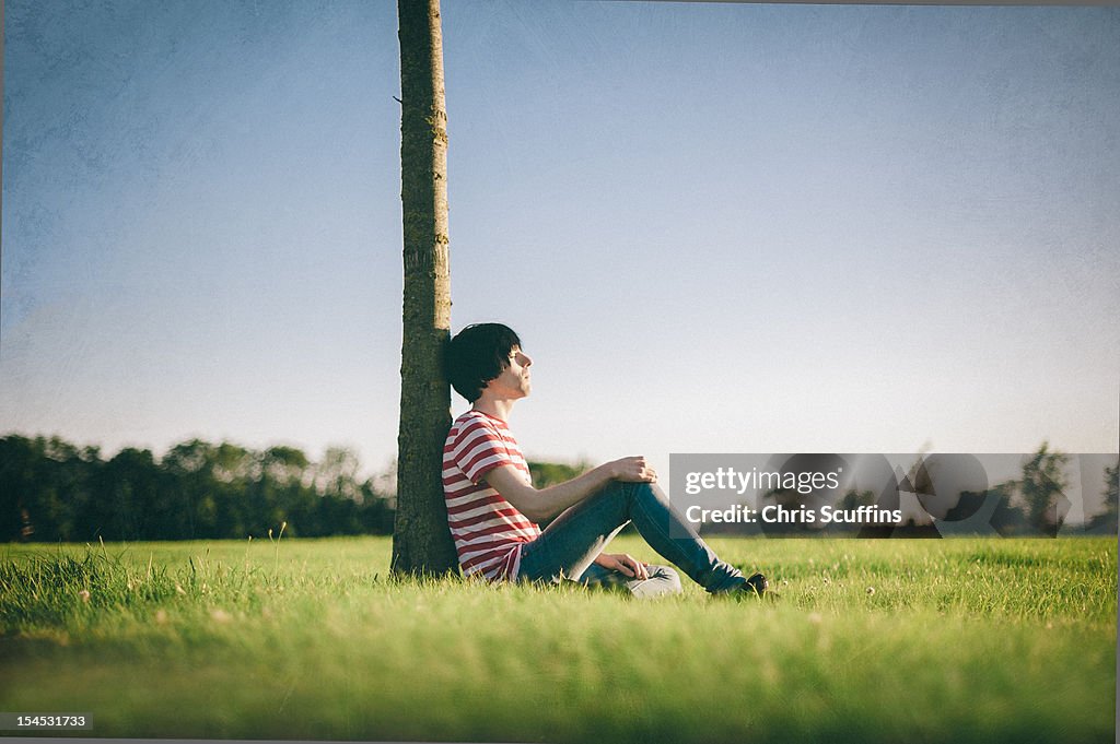 A Boy Thinking Beside A Tree