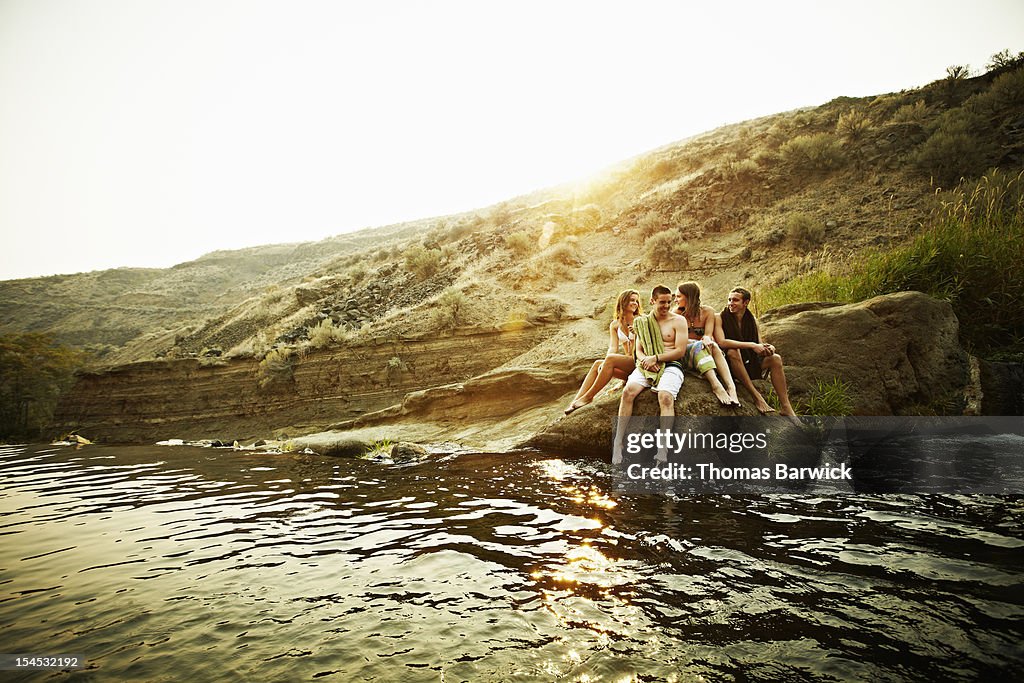Group of teenage friends sitting on rock at sunset