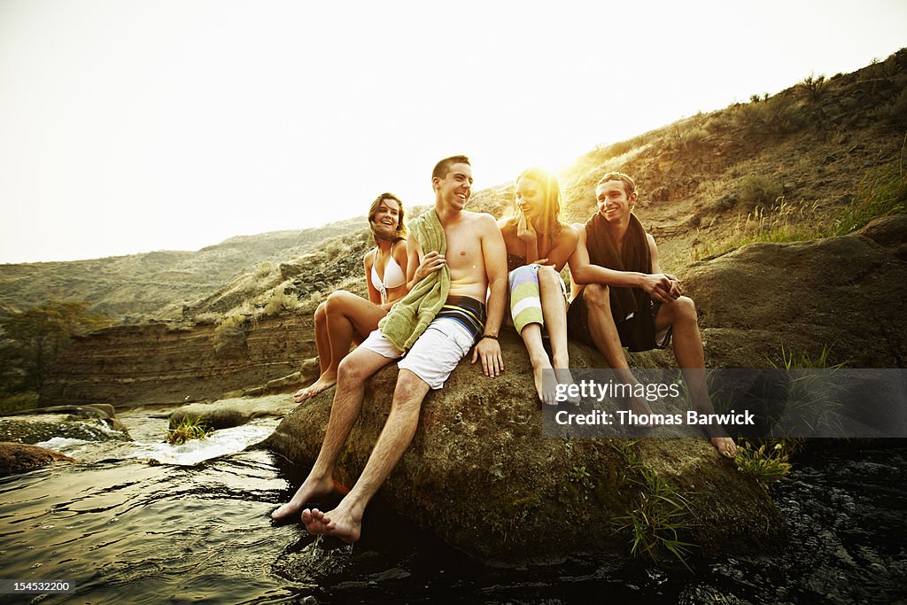 Teenage friends sitting on rock at sunset smiling