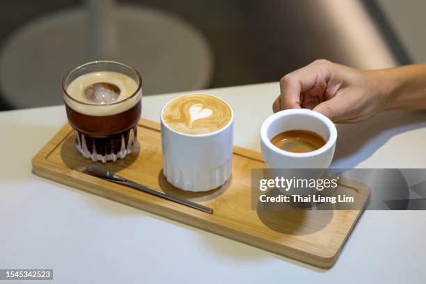 aus der nähe nimmt ein holztablett drei tassen auf, die jeweils eine einzigartige kaffeevariante enthalten - espresso, latte und eisschwarzer kaffee. - espresso stock-fotos und bilder