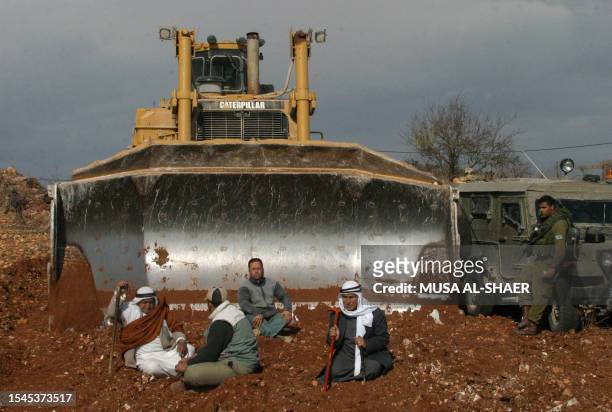 Palestinian farmers sit in front of a digger being protected by the Israeli military as they protest against the construction of Israel's...