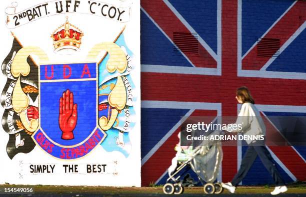 Woman pushes a pram past a loyalist mural showing a union flag and Ulster Freedom Fighters logo in a protestant area of Belfast 11 December 2000. U.S...