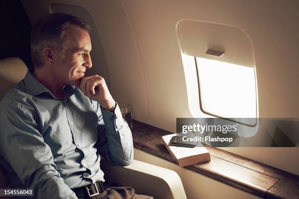 businessman gazing out of window aboard flight - aviacion fotografías e imágenes de stock