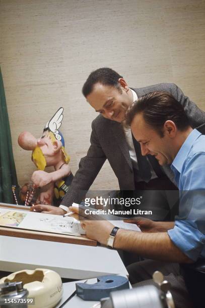Albert UDERZO home in Neuilly-sur-Seine: the artist sitting at his drawing board, a cigarette in hand, reading a document with his accomplice Rene...