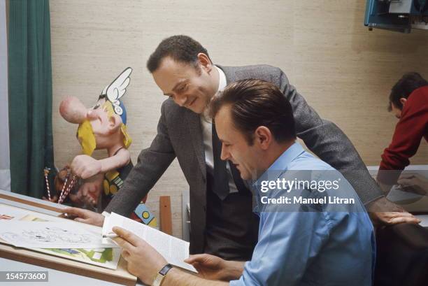 Albert UDERZO home in Neuilly-sur-Seine: the artist sitting at his drawing board, a cigarette in hand, reading a document with his accomplice Rene...