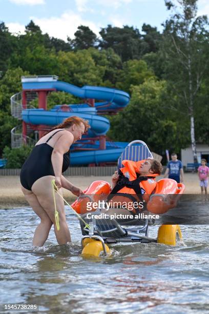 July 2023, Saxony-Anhalt, Arendsee: Anja Reisgies from the Herbert Feuchte Foundation Association pulls Emilie in a floatable wheelchair for a swim...