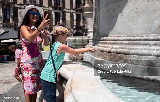 Mother photographs her child playing with water in the Elephant fountain in Piazza Duomo to seek refreshment on this hot day on July 15, 2023 in...