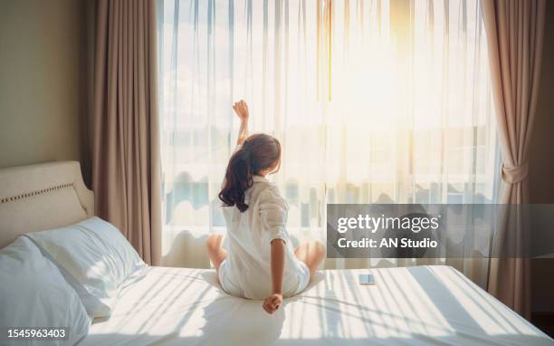 asian woman get up stretching relax in bed room at home. early out morning and wake up rest sunny day. lifestyle concept - rear view hand window stock pictures, royalty-free photos & images