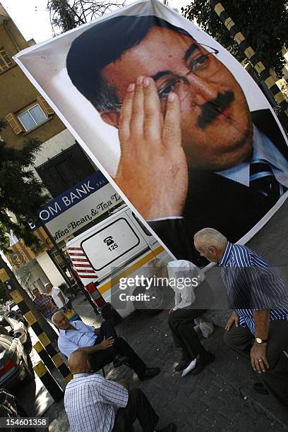 Lebanese men sit next to a poster of slain police intelligence chief General Wissam al-Hassan on October 23, 2012 near the site of a car bomb blast...