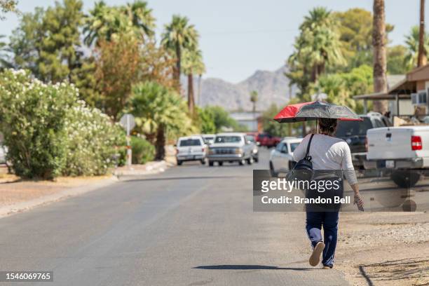 Person walks down the street with an umbrella during a heat wave on July 15, 2023 in Phoenix, Arizona. Weather forecasts today are expecting...