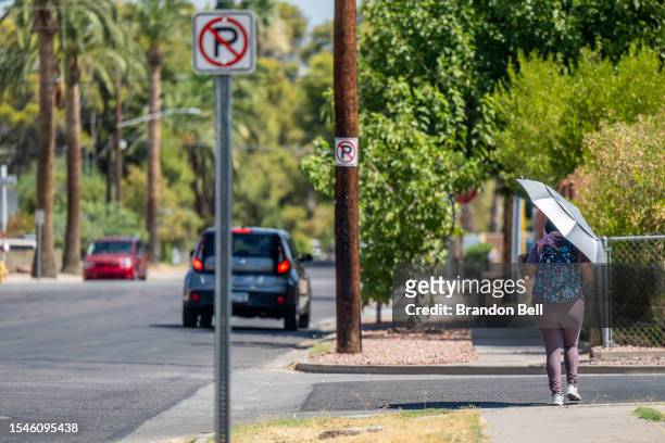 Person walks down the street with an umbrella during a heat wave on July 15, 2023 in Phoenix, Arizona. Weather forecasts today are expecting...
