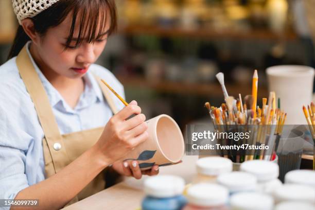 young asian potter artist painting a handmade ceramic cup in the studio - east asian works of art specialist stock pictures, royalty-free photos & images