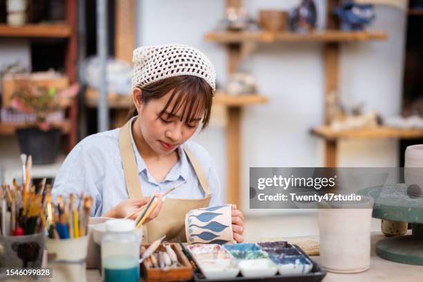 young asian potter artist painting a handmade ceramic cup in the studio - east asian works of art specialist stock pictures, royalty-free photos & images
