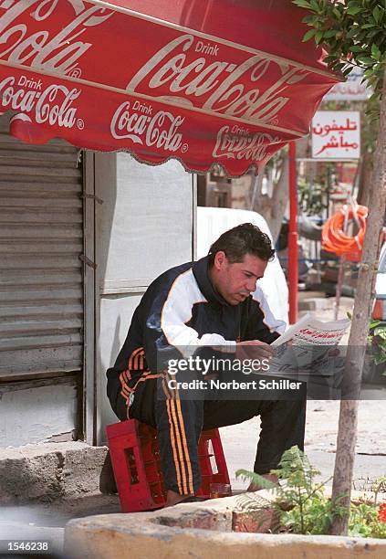 An Egyptian man reads an opposition newspaper below an advertisement for Coca Cola, May 30, 2002 in Cairo. Egypt's opposition press has featured many...