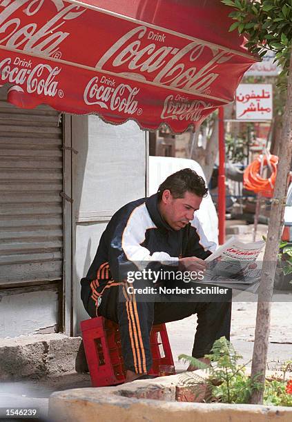 An Egyptian man reads an opposition newspaper below an advertisement for Coca Cola, May 30, 2002 in Cairo. Egypt's opposition press has featured many...