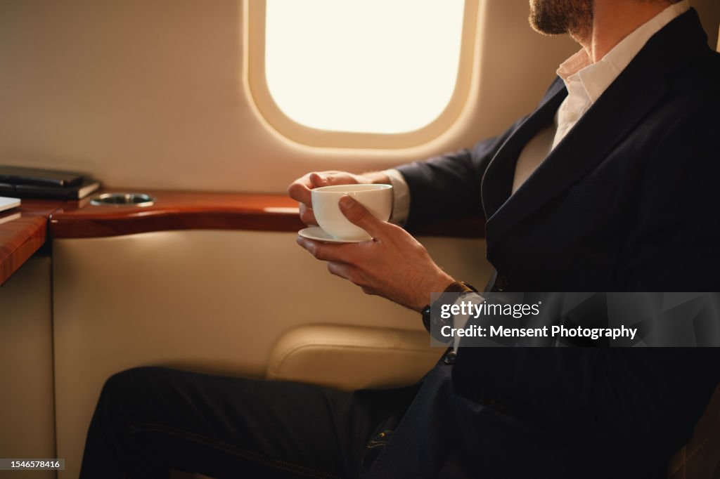 Unrecognizable elegant CEO businessman traveler drinks coffee while in flight in the first-class private airplane jet