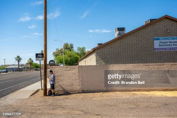 Resident Adrian Mata stands behind a pole for shade while waiting for the bus during a heat wave on July 15, 2023 in Phoenix, Arizona. Weather...