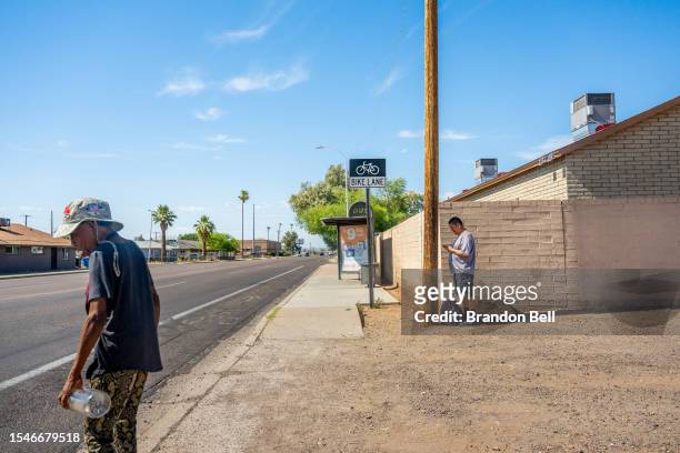 Resident Adrian Mata stands behind a pole for shade while waiting for the bus during a heat wave on July 15, 2023 in Phoenix, Arizona. Weather...