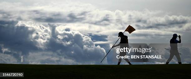 Japan's Takumi Kanaya walk off the green as his caddie Lionel Matichuk replaces the 12th green flag, backdropped by rain clouds building on the...