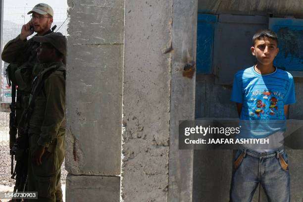 Israeli troops stand guard at the Hawara checkpoint near the West Bank city of Nablus with an arrested Palestinian youth standing on the right after...