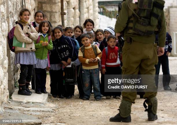 An Israeli soldier prevents the passage of Palestinian school children watching Israelis parade in celebration of the Jewish holiday of Purim in the...