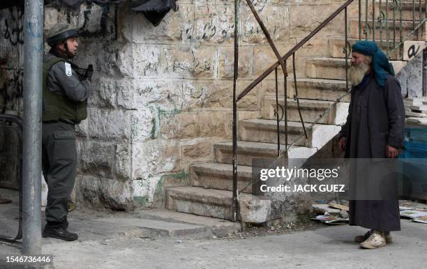 Palestinian man looks at an Israeli soldier patroling a street during clashes with stone throwers in the area of the Ibrahimi Mosque or the Tomb of...