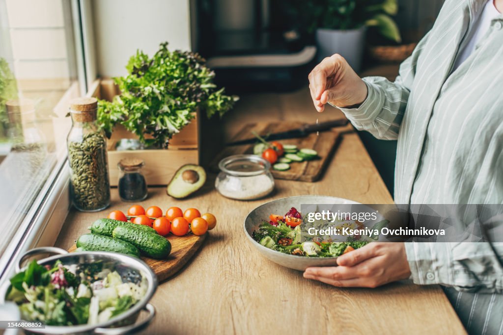 Woman mixing delicious superfood salad ingredients with wooden spoons in kitchen