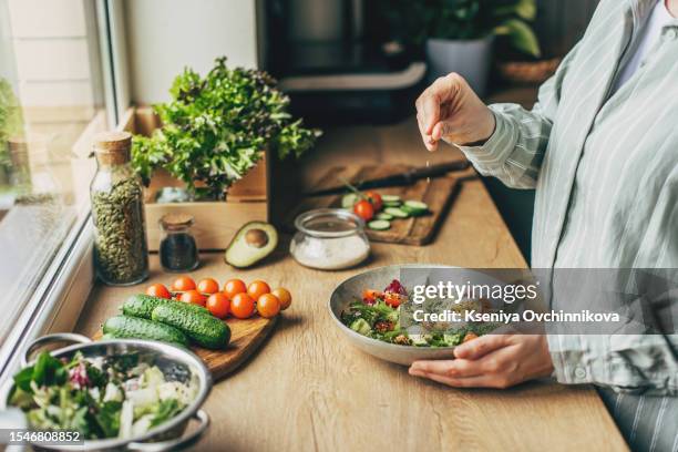 woman mixing delicious superfood salad ingredients with wooden spoons in kitchen - préparation des aliments photos et images de collection