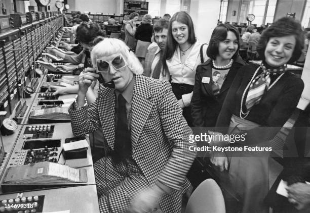 English dj and television presenter Jimmy Savile making a call from the Wren House International Telephone Exchange in London, 14th April 1975....