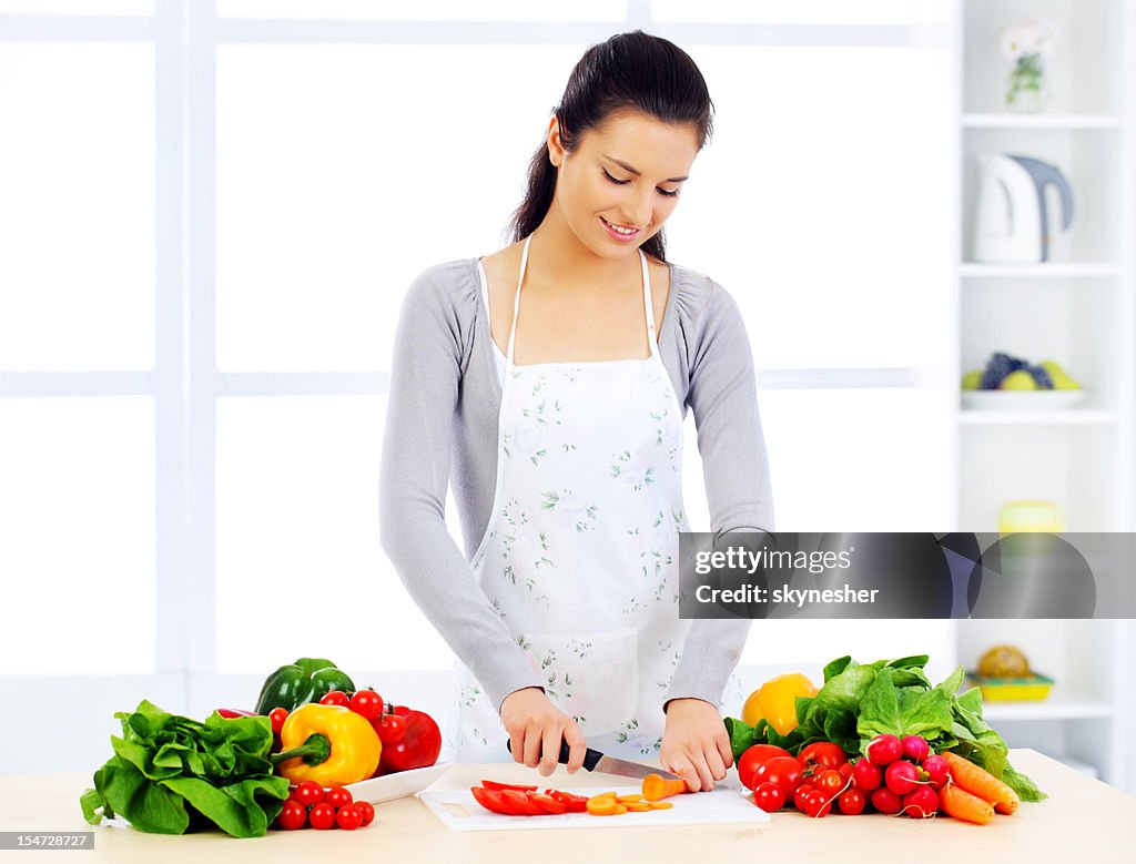Pretty girl in her kitchen cutting vegetable ingredients.