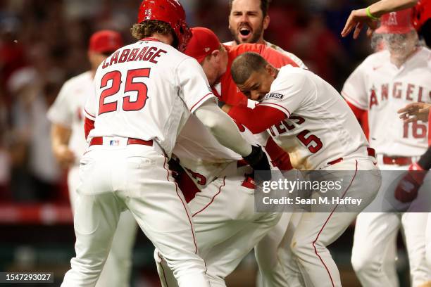 Trey Cabbage and Eduardo Escobar congratulate Taylor Ward of the Los Angeles Angels after he grounded into a fielders choice scoring the go ahead run...