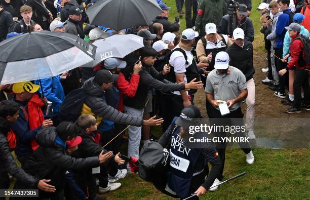 Fans try to touch US golfer Max Homa and Northern Ireland's Rory McIlroy as they walk to the 13th tee on day three of the 151st British Open Golf...