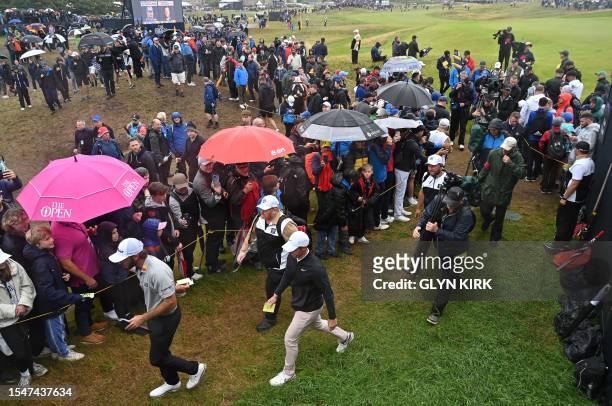 Fans try to touch US golfer Max Homa and Northern Ireland's Rory McIlroy as they walk to the 13th tee on day three of the 151st British Open Golf...