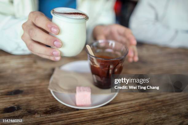 the asian boy  holds a small glass of hot milk in his hand, which is about to be mixed with hot chocolate and turned into hot chocolate milk - chocolate milk splash stock pictures, royalty-free photos & images