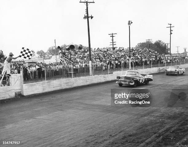 April 29, 1956: Bob Welborn takes the checkered flag to win the NASCAR Convertible Division race at Greensboro Fairgrounds over second-finisher Gwyn...