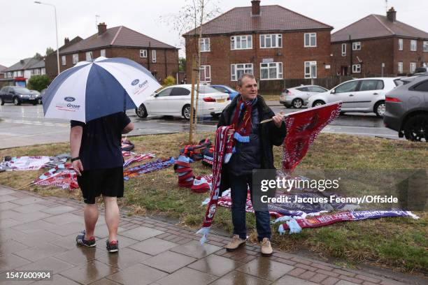 Merchandise seller stands in the rain during the pre-season friendly match between Dagenham & Redbridge and West Ham United at Chigwell Construction...