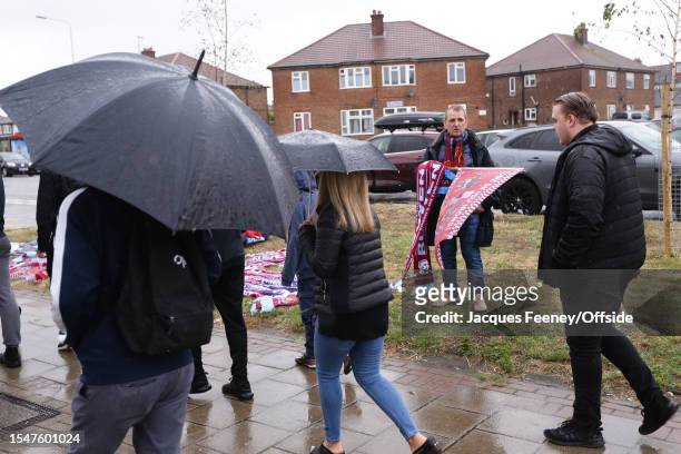 Merchandise seller stands in the rain during the pre-season friendly match between Dagenham & Redbridge and West Ham United at Chigwell Construction...