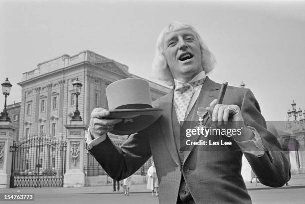 English dj and television presenter Jimmy Savile , showing off his OBE after his investiture at Buckingham Palace, London, 21st March 1972.