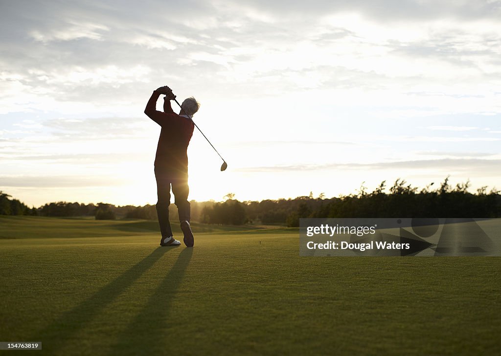 Senior golfer teeing off on golf course.