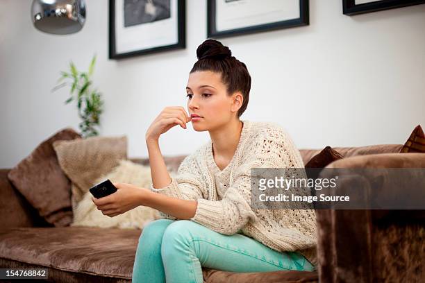 young woman sitting on sofa with smartphone - hand on chin thinking stock pictures, royalty-free photos & images