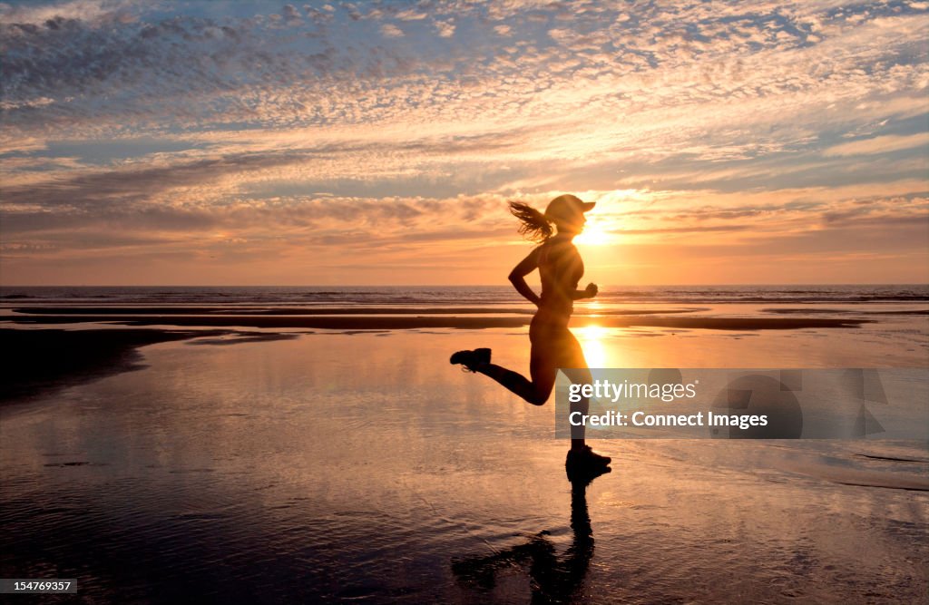 Woman running on beach at sunrise