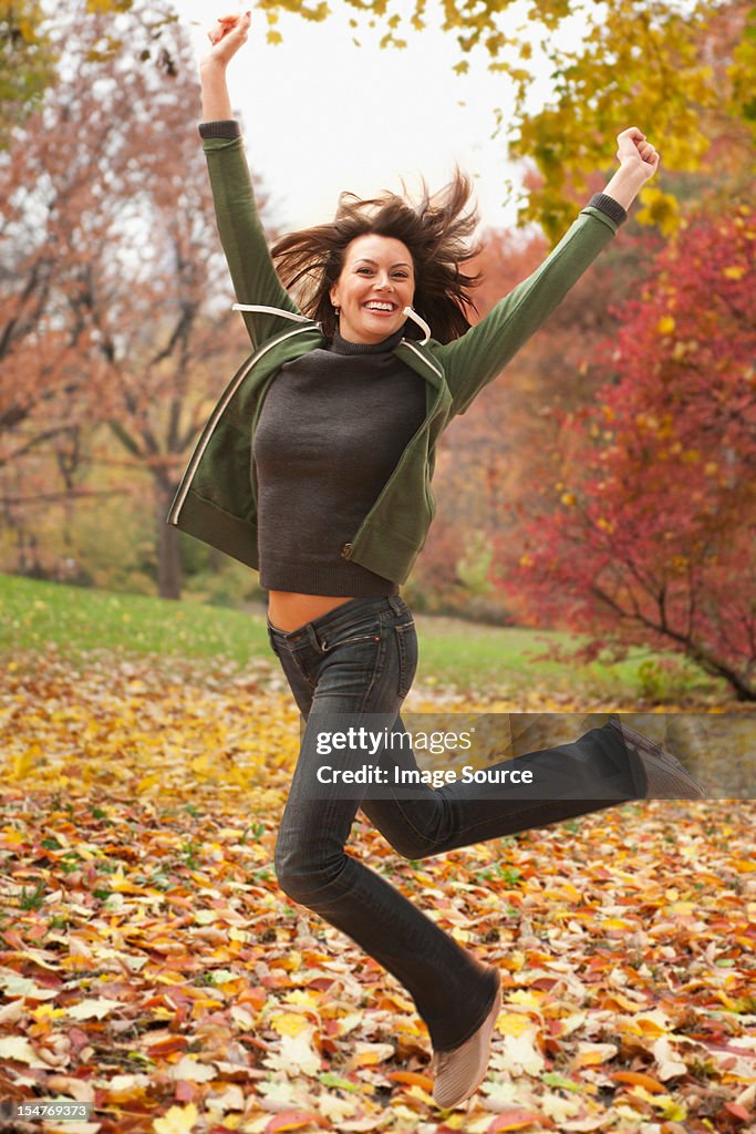 Woman jumping in autumn leaves