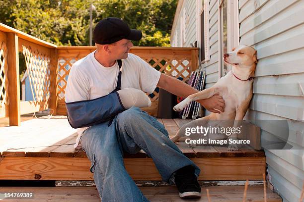 man outside house with arm in sling and dog - cabestrillo de brazo fotografías e imágenes de stock