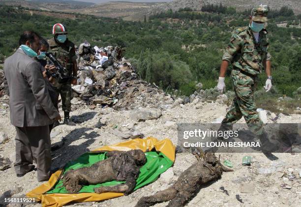 Syrian soldiers and a cameraman gather around human remains which the government said were found at a mass grave in Jisr al-Shughur, 325 kms...